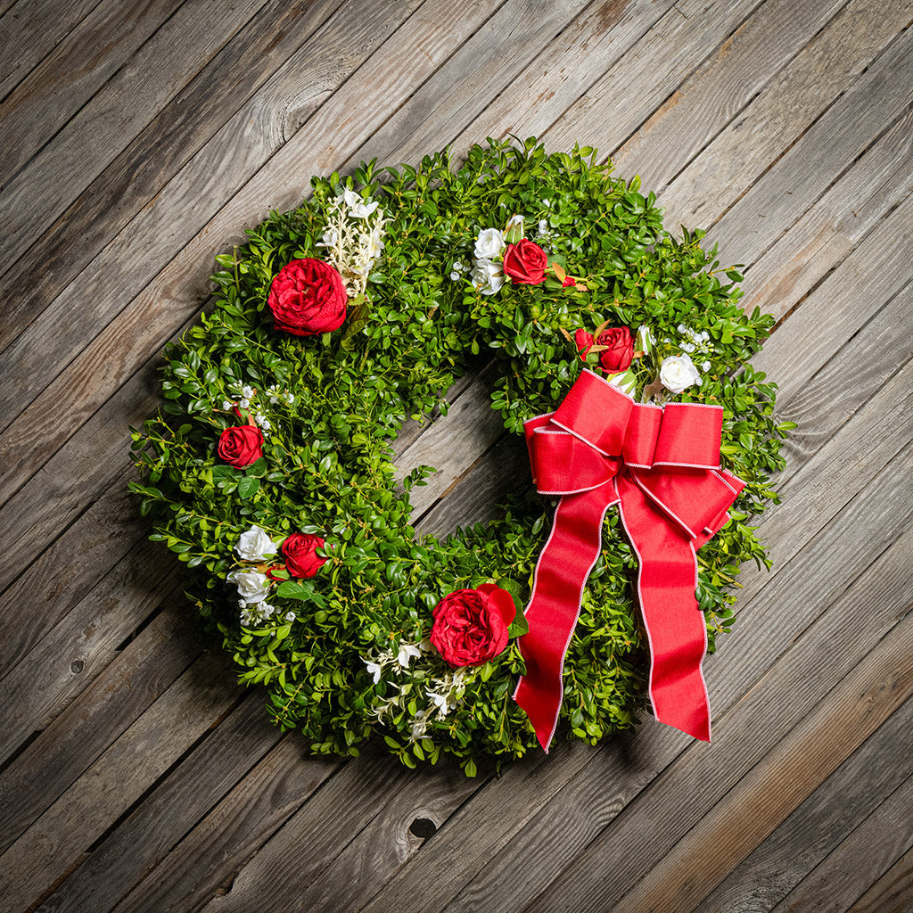 Fresh boxwood with faux red roses, faux white roses, and other faux white flowers with a red and pink-back bow