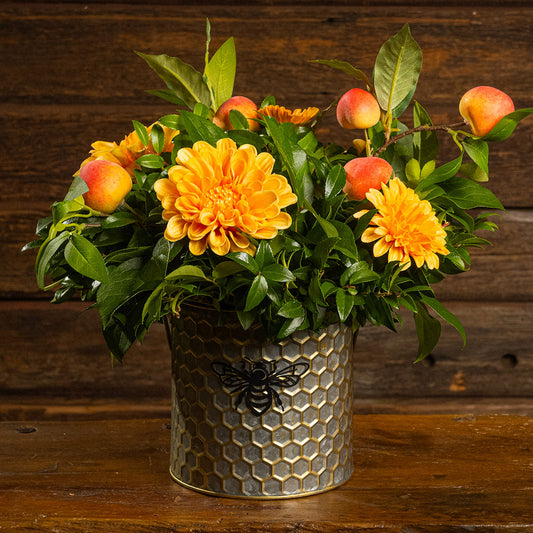 Fresh salal and green huckleberry with faux orange dahlia flowers and peach branches in a metal honeycomb pot with a honey bee