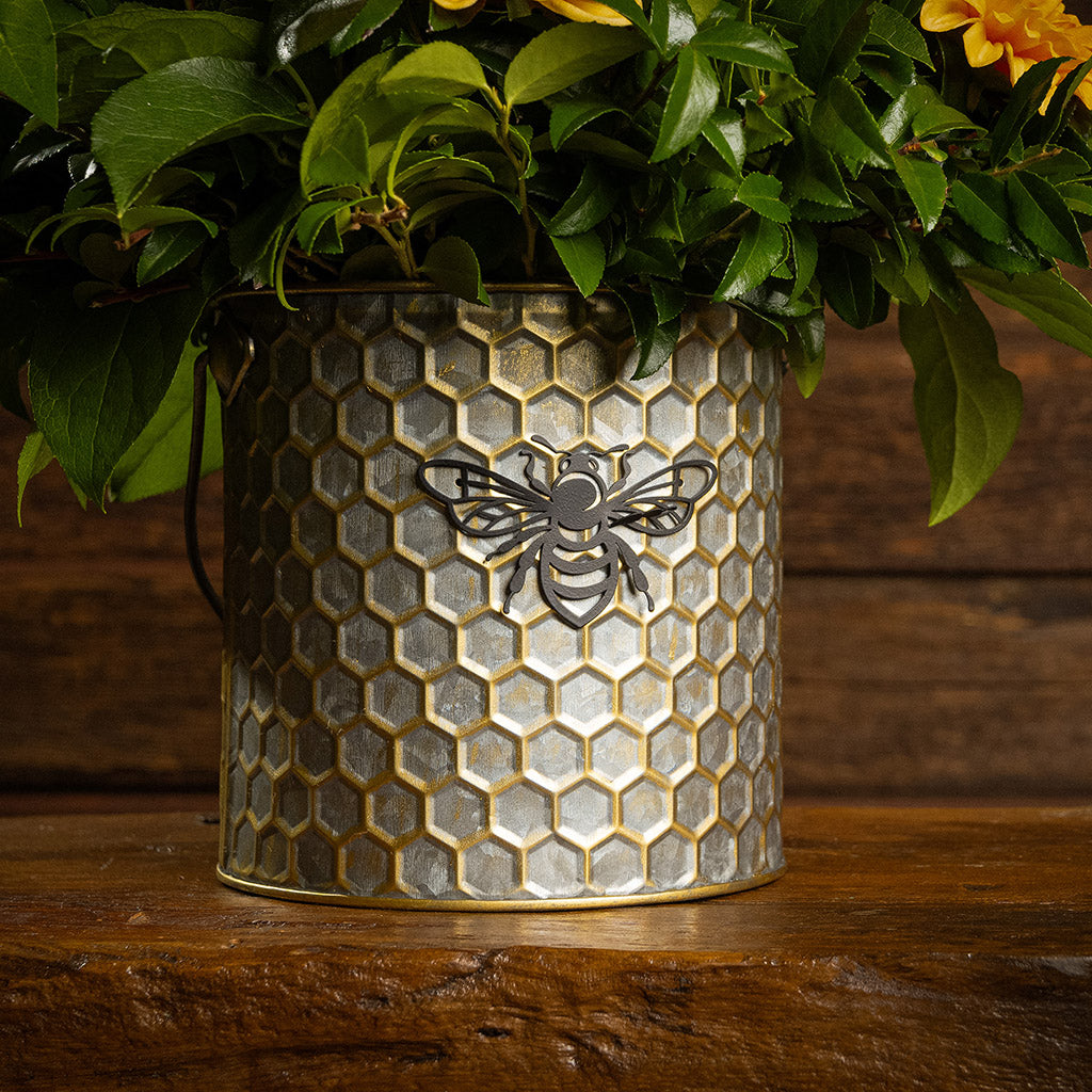 Fresh salal and green huckleberry with faux orange dahlia flowers and peach branches in a metal honeycomb pot with a honey bee