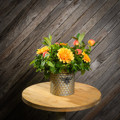 Fresh salal and green huckleberry with faux orange dahlia flowers and peach branches in a metal honeycomb pot with a honey bee