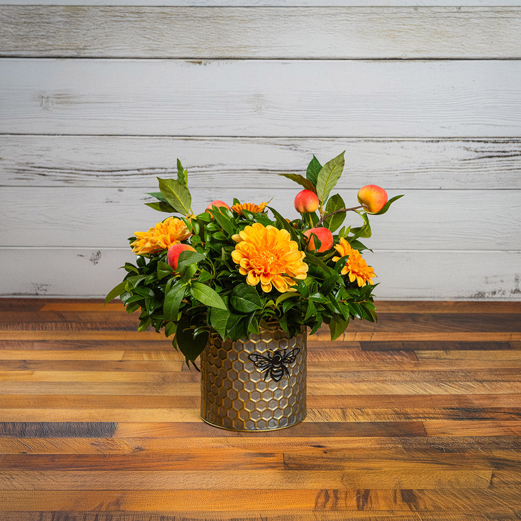 Fresh salal and green huckleberry with faux orange dahlia flowers and peach branches in a metal honeycomb pot with a honey bee