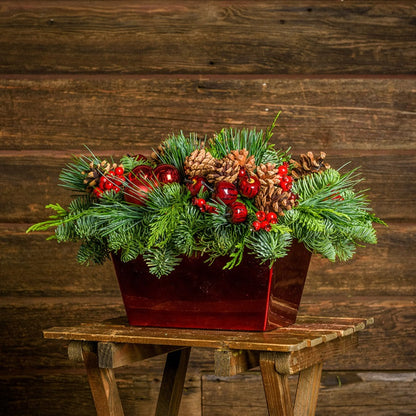 Centerpiece made of noble fir, cedar, and pine with Australian pine cones, red berry clusters, apple/pine cone picks, and a red metallic container