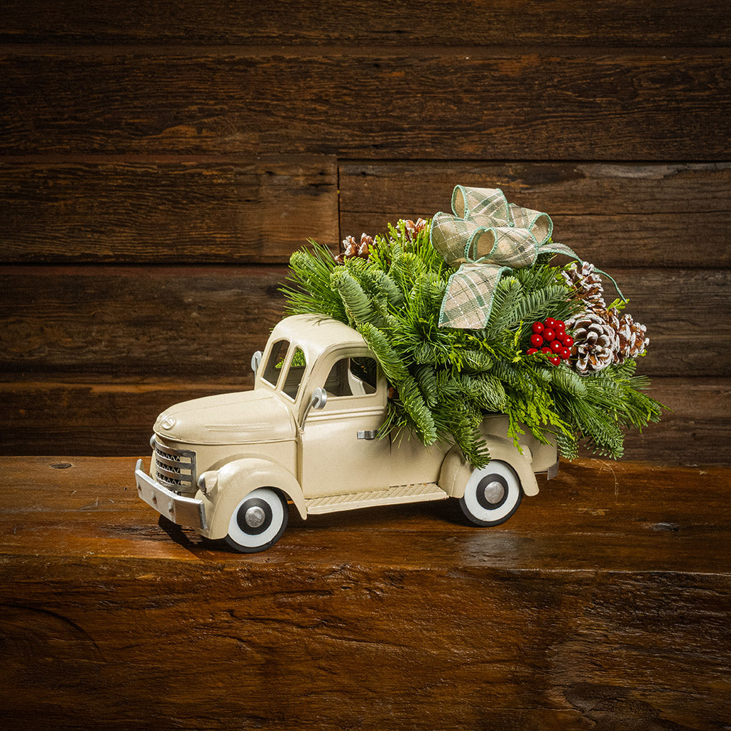 noble fir, cedar, and pine with faux red berries, frosted pinecones, and a sage plaid bow in a cream metal truck container