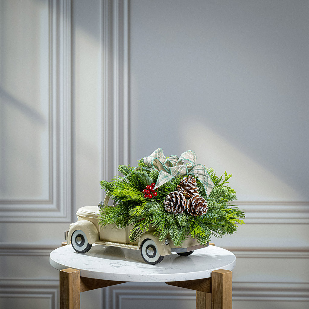 noble fir, cedar, and pine with faux red berries, frosted pinecones, and a sage plaid bow in a cream metal truck container
