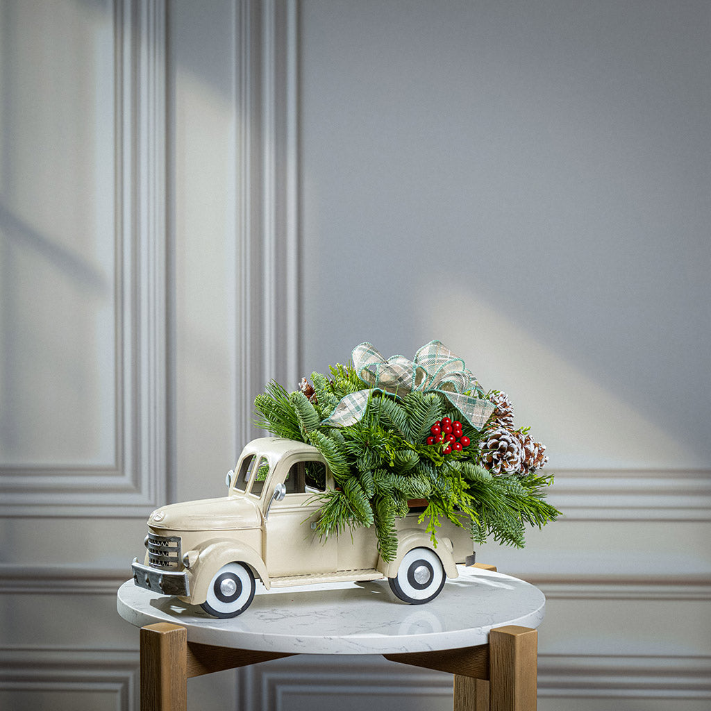 noble fir, cedar, and pine with faux red berries, frosted pinecones, and a sage plaid bow in a cream metal truck container
