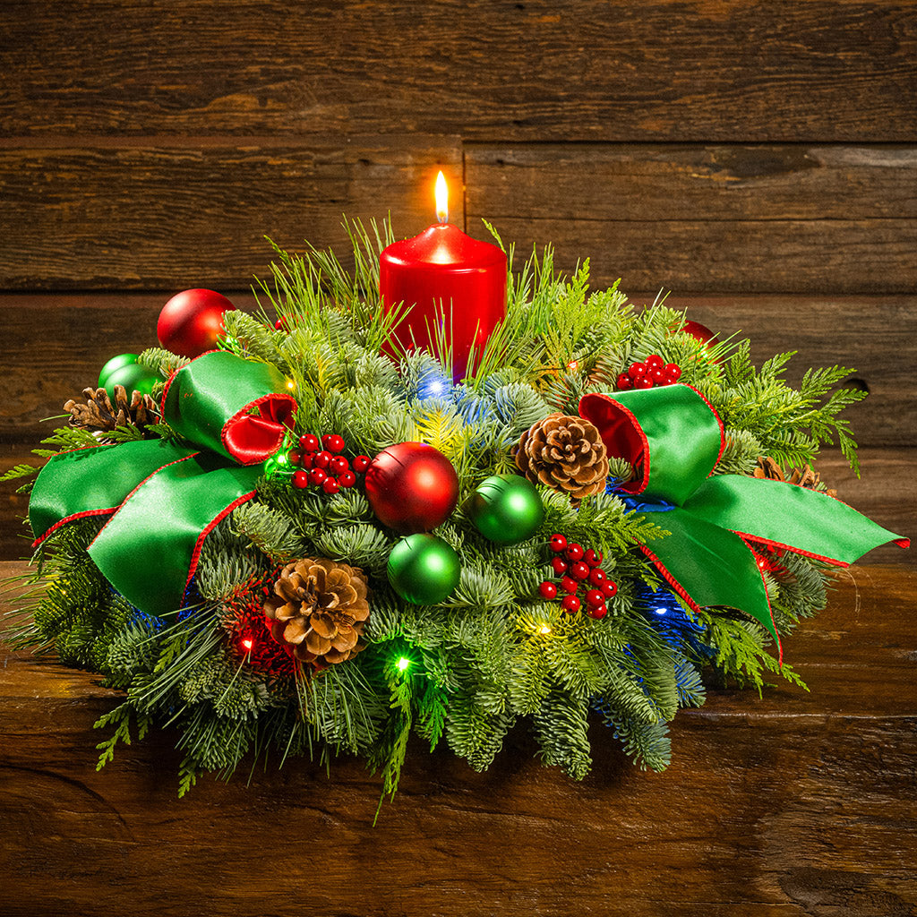 Decorative Christmas wreath with red and green ornaments and a lit candle on a wooden surface.