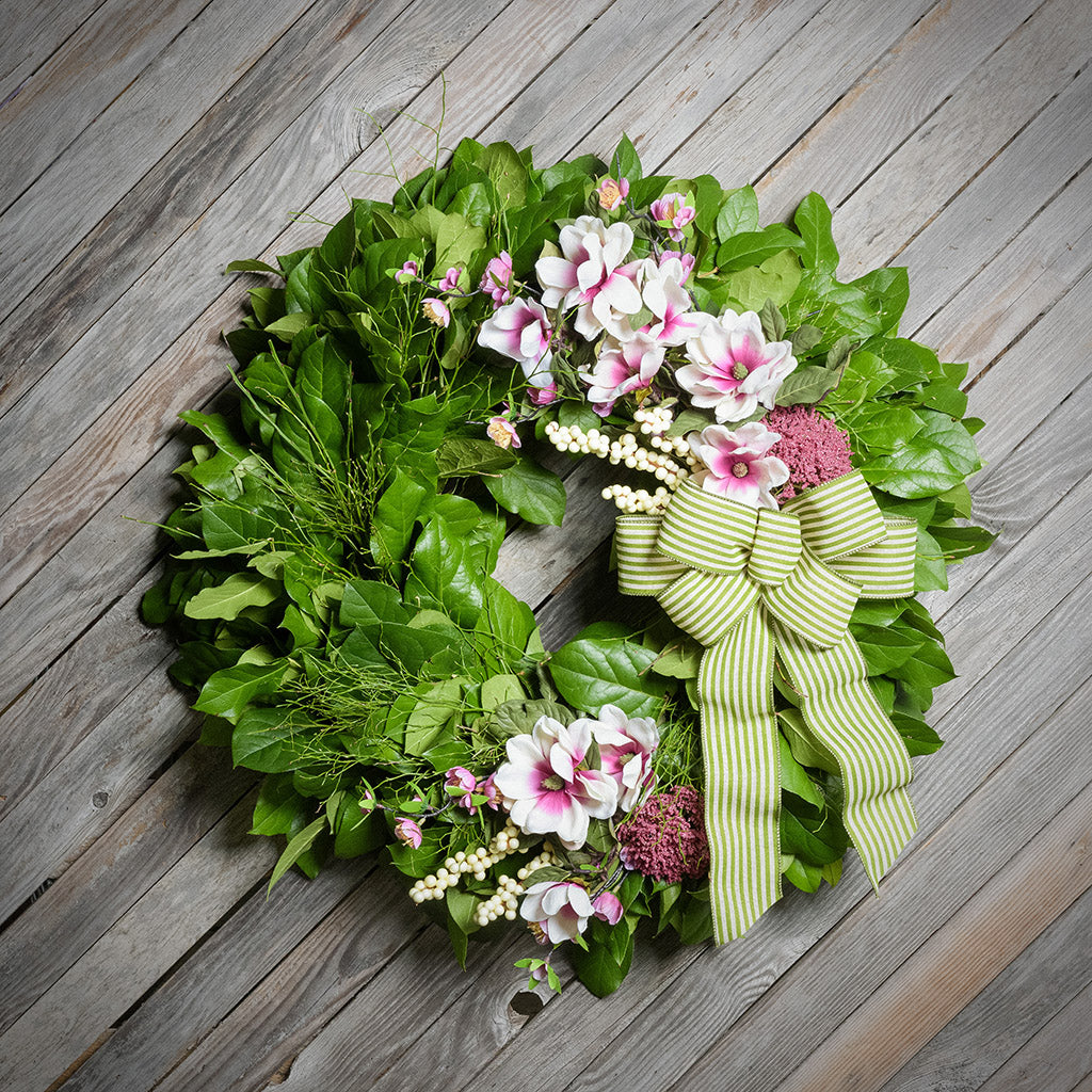 Floral wreath with a green and white striped bow on a wooden surface