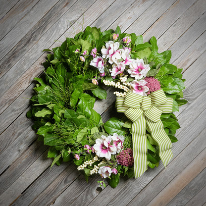 Floral wreath with a green and white striped bow on a wooden surface