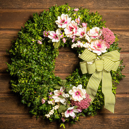 Fresh boxwood with faux pink and ivory magnolia flowers, faux cherry blossoms, faux cream berries, and faux pink Queen Anne’s lace flowers with a sage-green and ivory striped bow