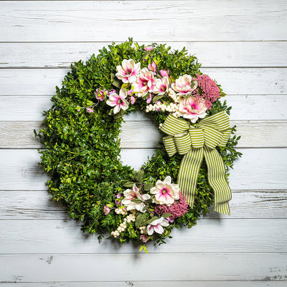 Fresh boxwood with faux pink and ivory magnolia flowers, faux cherry blossoms, faux cream berries, and faux pink Queen Anne’s lace flowers with a sage-green and ivory striped bow