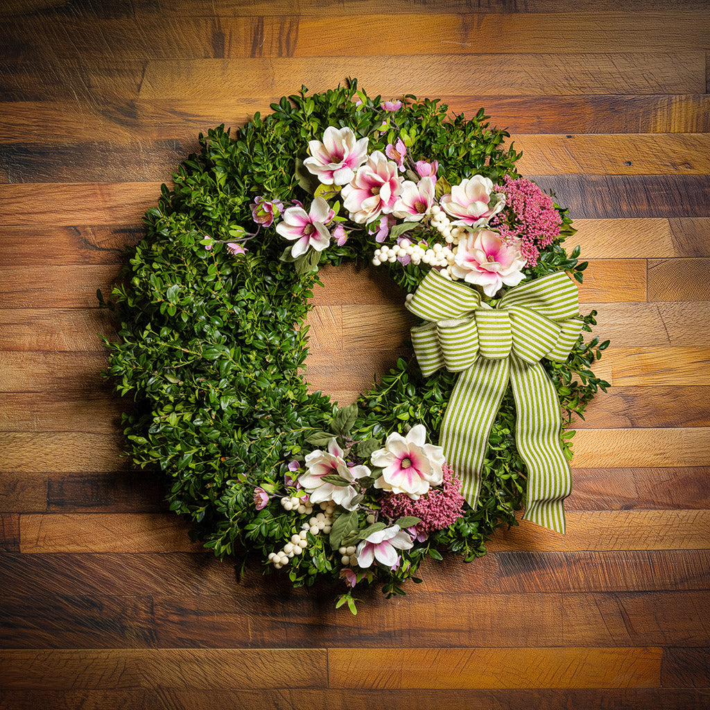 Fresh boxwood with faux pink and ivory magnolia flowers, faux cherry blossoms, faux cream berries, and faux pink Queen Anne’s lace flowers with a sage-green and ivory striped bow