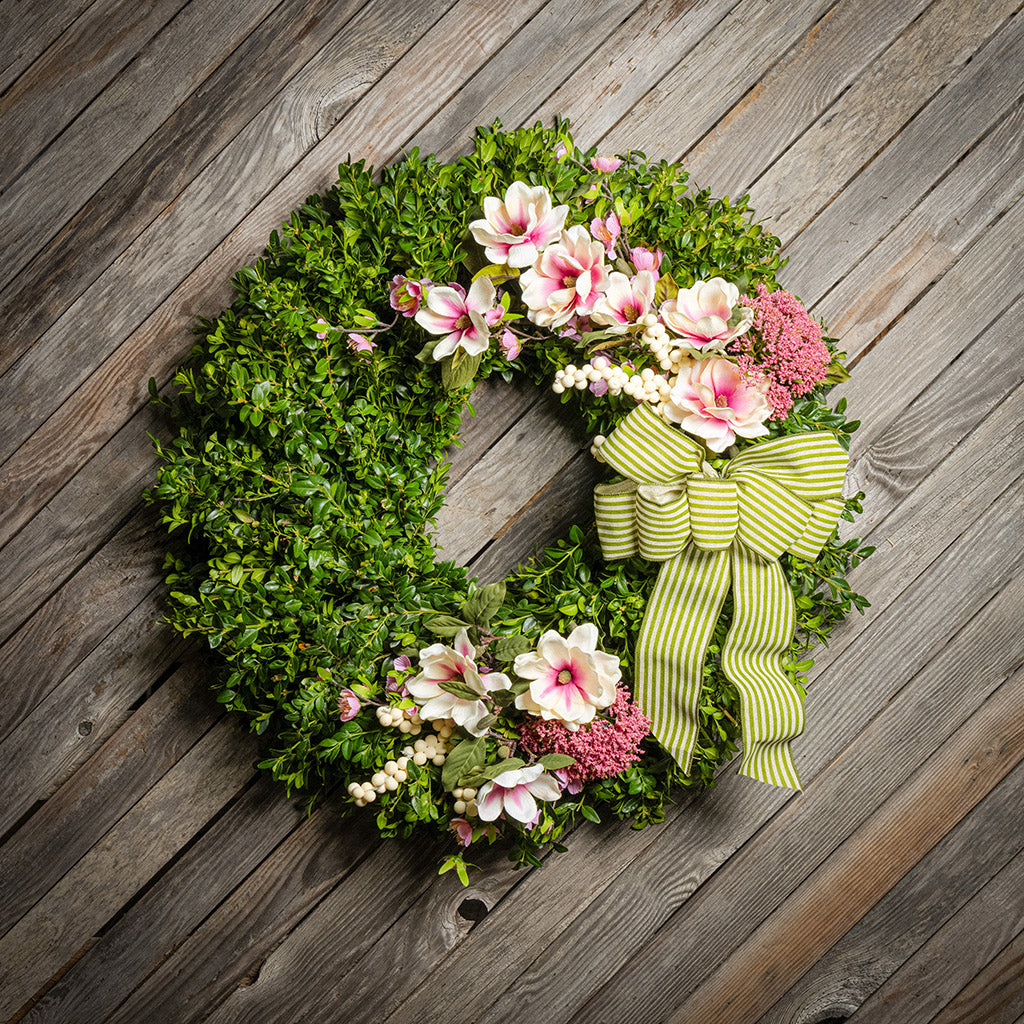 Fresh boxwood with faux pink and ivory magnolia flowers, faux cherry blossoms, faux cream berries, and faux pink Queen Anne’s lace flowers with a sage-green and ivory striped bow