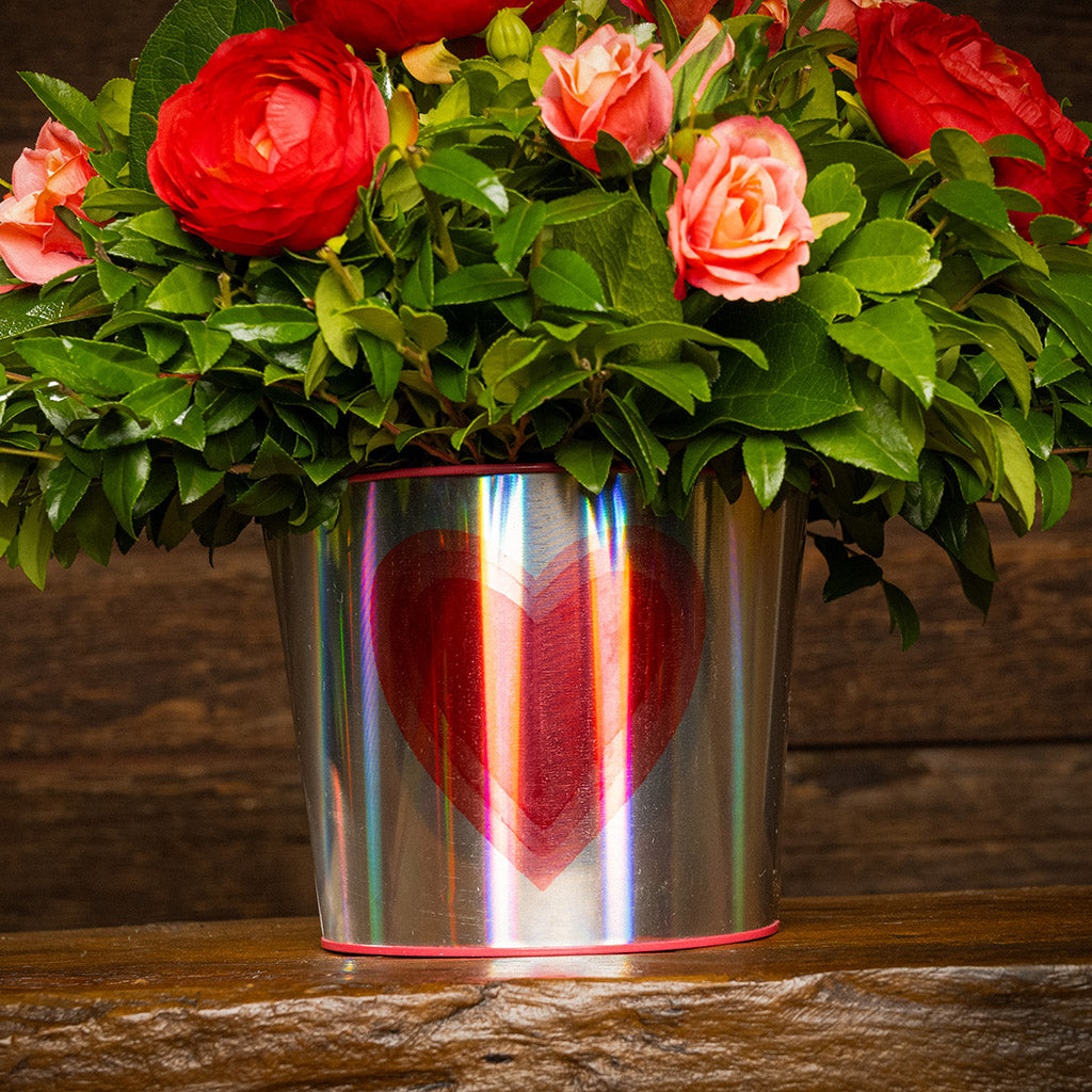 Salal and huckleberry with faux red ranunculus flowers and faux peach roses in a silver metal container adorned with hearts