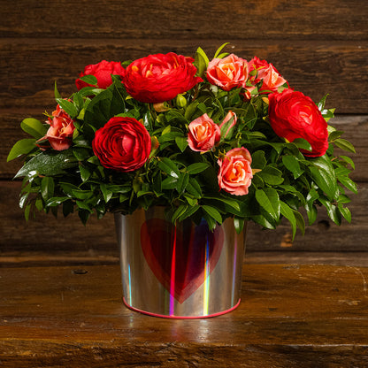 Salal and huckleberry with faux red ranunculus flowers and faux peach roses in a silver metal container adorned with hearts