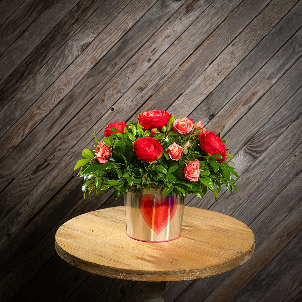 Salal and huckleberry with faux red ranunculus flowers and faux peach roses in a silver metal container adorned with hearts