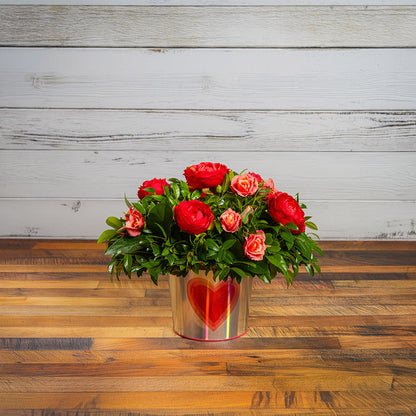 Salal and huckleberry with faux red ranunculus flowers and faux peach roses in a silver metal container adorned with hearts