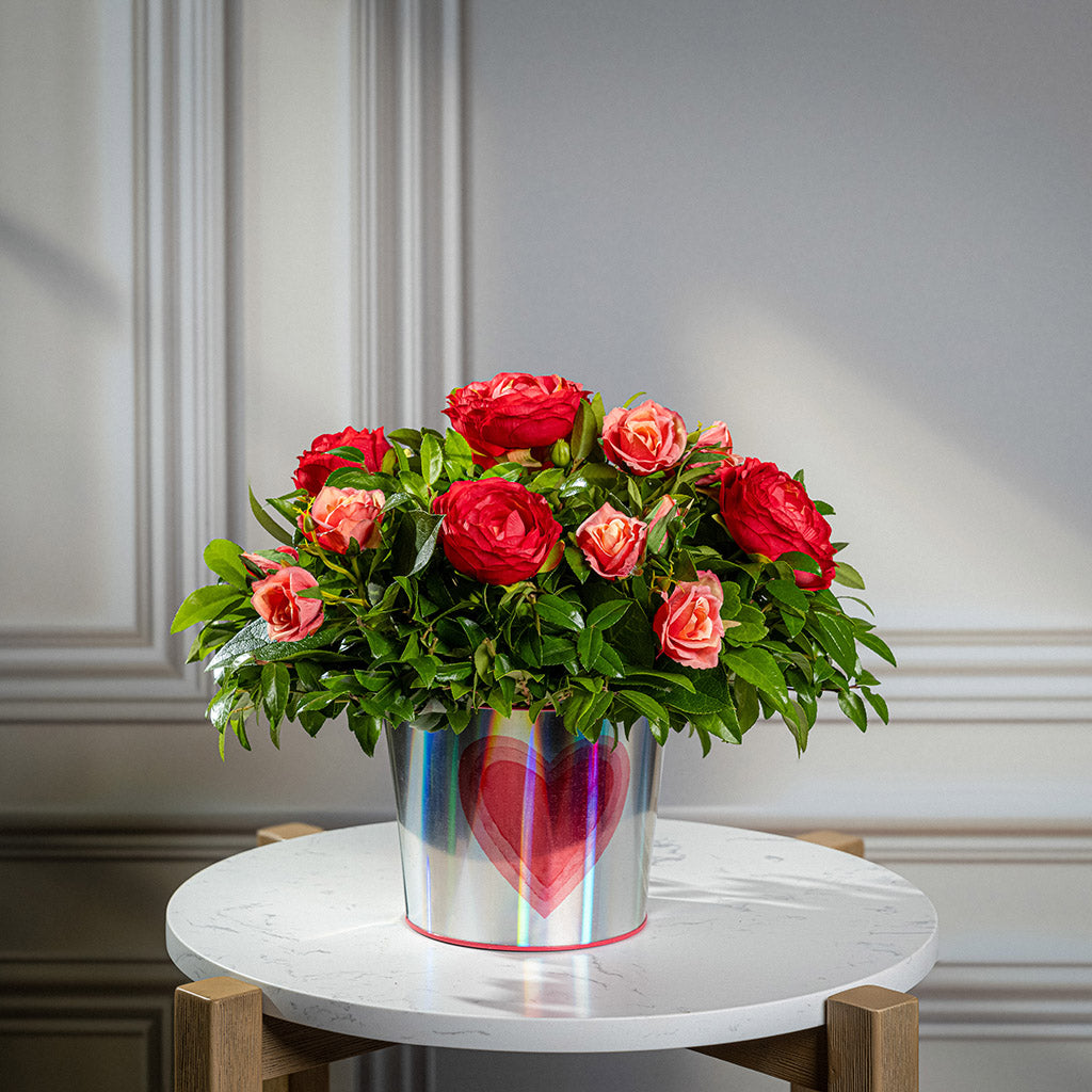 Salal and huckleberry with faux red ranunculus flowers and faux peach roses in a silver metal container adorned with hearts