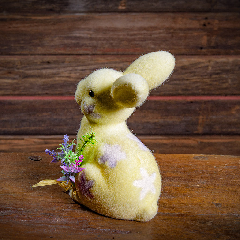 Yellow soft rabbit with flowers on a wooden surface