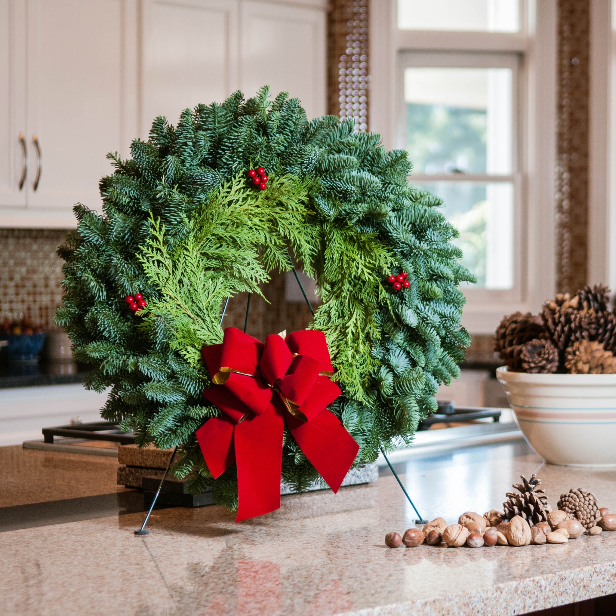 Christmas wreath of fir and cedar with three red berry clusters and a gold-backed red velveteen bow on kitchen counter