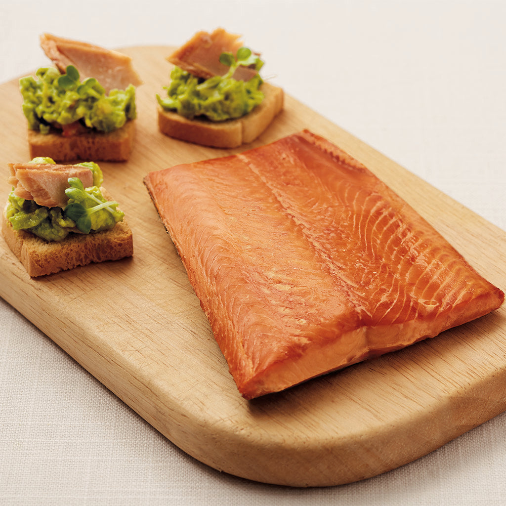 Smoked salmon on toast with a green paste sitting on a wooden cutting board.