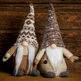 14” Gnomes weighted at the bottom with their noses poking out of tall brown and white pointy hats, their fuzzy white beards, and brown linen outfits sitting on a wood table with a dark wood background.