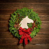 Christmas wreath made of noble fir and cedar with a wooden horse head cutout, 4 pine cones, red berry clusters, and a red brushed linen bow on a dark wood background.