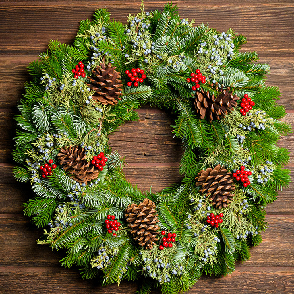 A wreath made of Nordmann fir and juniper with ponderosa pine cones and red berries with a dark wooden background.