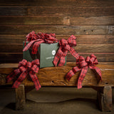 6 Red and Black plaid bows shown with a green shipping box sitting on a wood bench with a dark wood wood background.