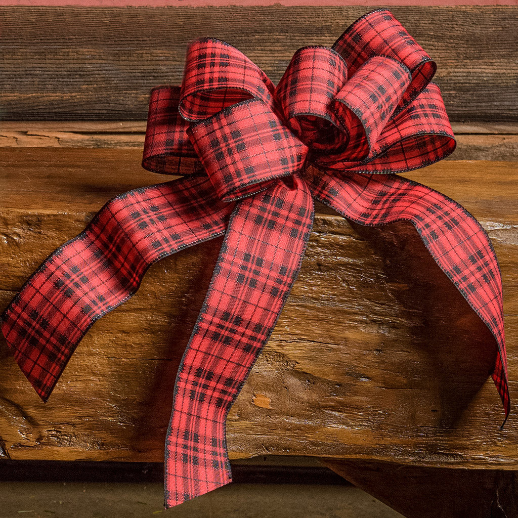 Red and Black plaid bow sitting on a wood bench with a dark wood background.