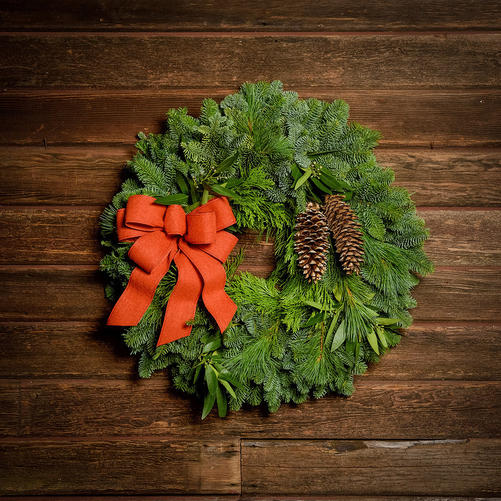 Christmas wreath with bay leaves, pine cones with an orange brushed linen bow on a dark wood background.