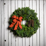 Christmas wreath with bay leaves, pine cones with an orange brushed linen bow on a white wood background.