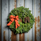 Christmas wreath with bay leaves, pine cones with an orange brushed linen bow on a rustic metal background.