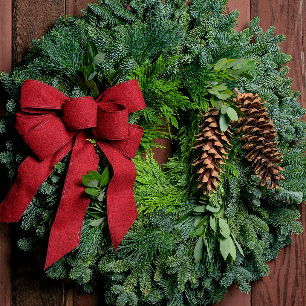 Christmas wreath with bay leaves, pine cones with an red brushed linen bow on a dark wood background.