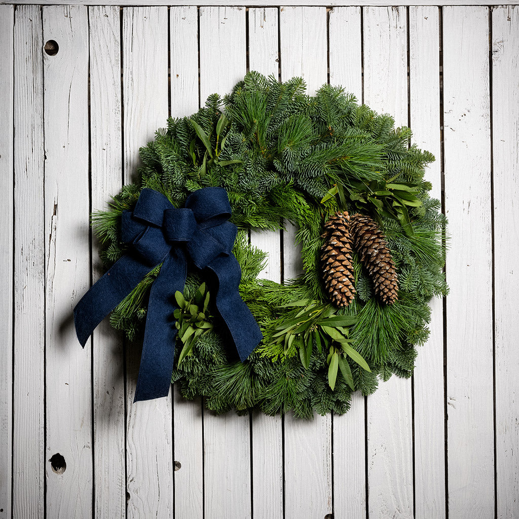 Christmas wreath with bay leaves, pine cones with a blue brushed linen bow on a white wood background.