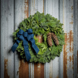 Christmas wreath with bay leaves, pine cones with a blue brushed linen bow on a rustic metal background.