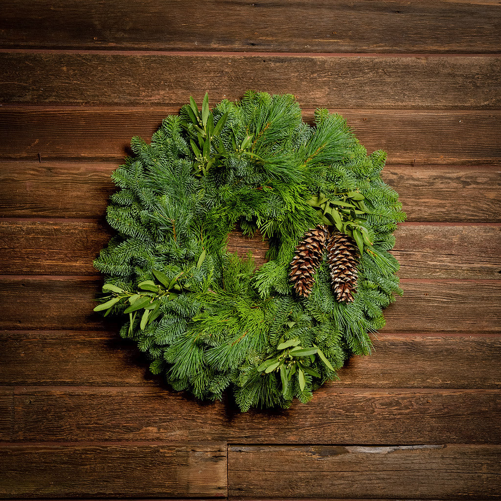 Christmas wreath with bay leaves, pine cones with no bow on a dark wood background.
