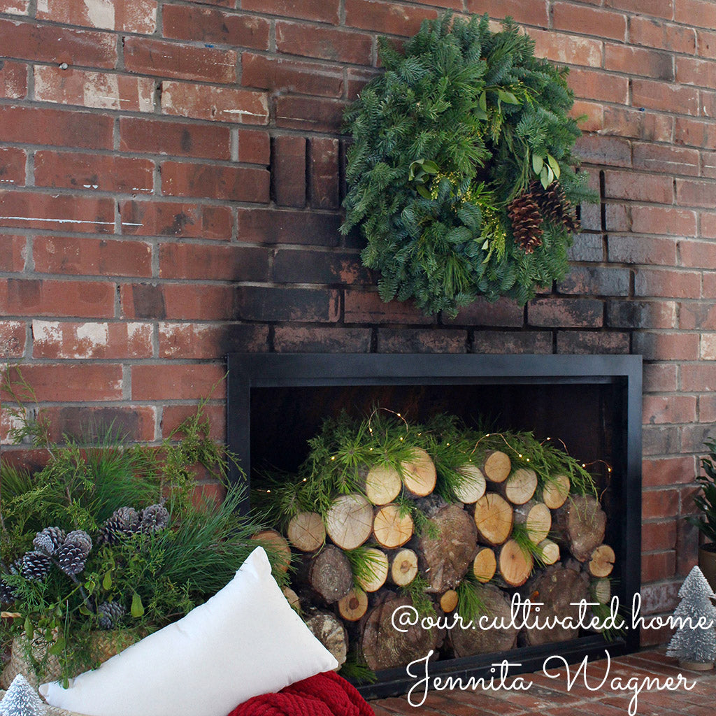 Christmas wreath with bay leaves, pine cones with no bow hung over a red brick fireplace.