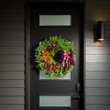 Holiday wreath made of noble fir, incense cedar, white pine, and bay leaf with purple and copper balls, gold pinecones and leaves, branches of multi-colored berries, and a purple velvet and shimmery copper double bow on a black door.