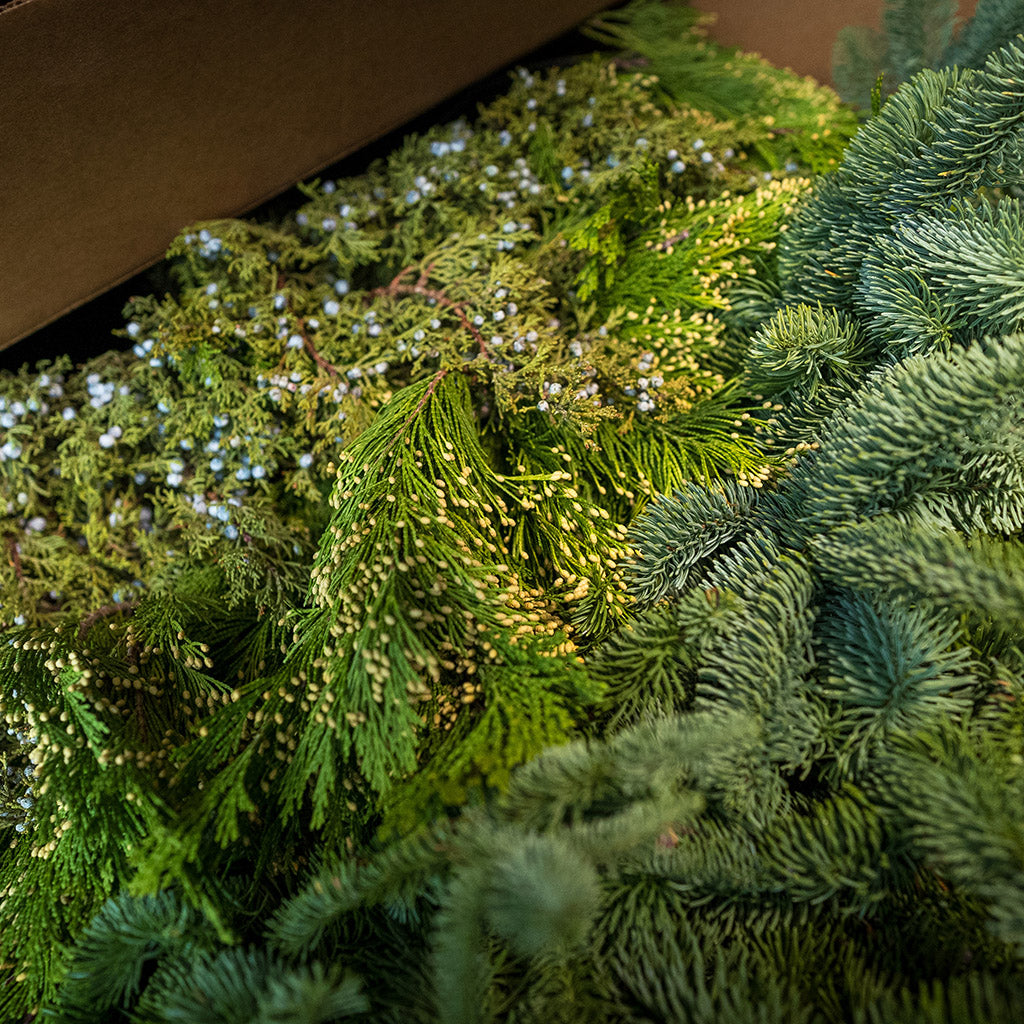 Close up of loosely boxed 14 lbs of Noble Fir in 6"-24” length pieces, 3 lbs of Incense Cedar in 6" - 18" length pieces, and 3 lbs of Juniper in 6" - 12" length pieces laying on a front porch.