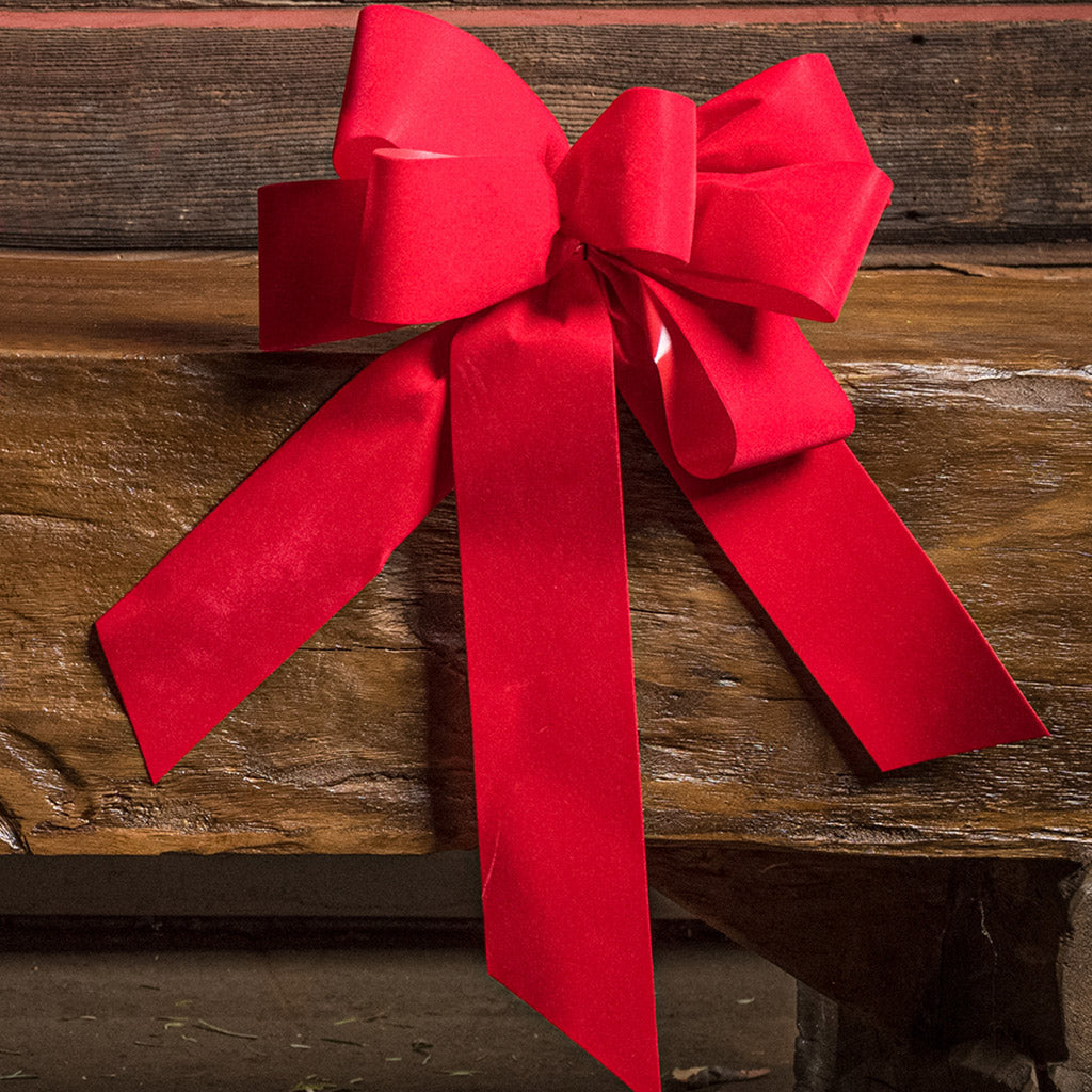 Bright Red bow shown sitting on a wood bench with a dark wood background.