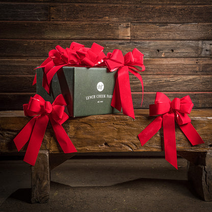 6 Bright Red bows shown with a green shipping box sitting on a wood bench with a dark wood background.