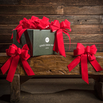 6 Bright Red bows shown with a green shipping box sitting on a wood bench with a dark wood background.