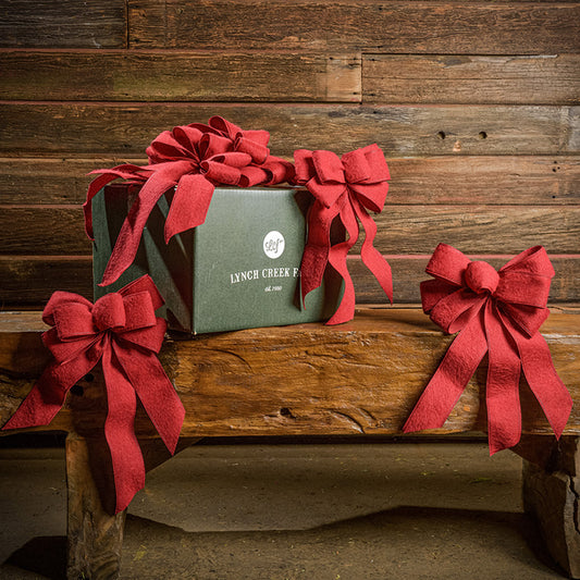 6 Brushed Linen Red bows shown with a green shipping box sitting on a wood bench with a dark wood background.