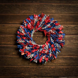22" botanical wreath is handmade with red and blue integrifolia leaves and white flax on a dark wood background.