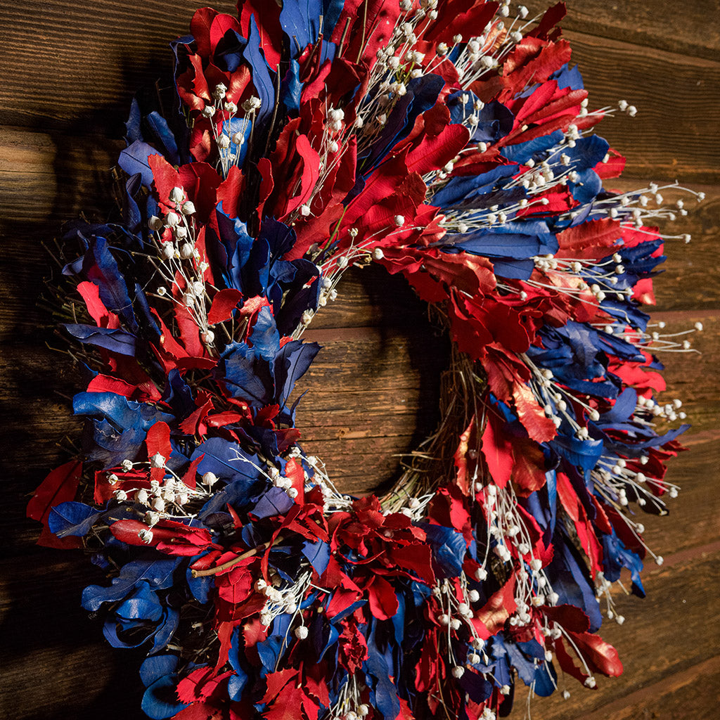 22" botanical wreath is handmade with red and blue integrifolia leaves and white flax on a dark wood background.