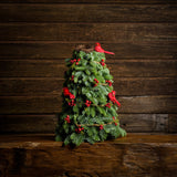 Tabletop tree of noble fir with a rustic berry garland, 3 cardinal birds, and a nest on a wooden table against a wood wall