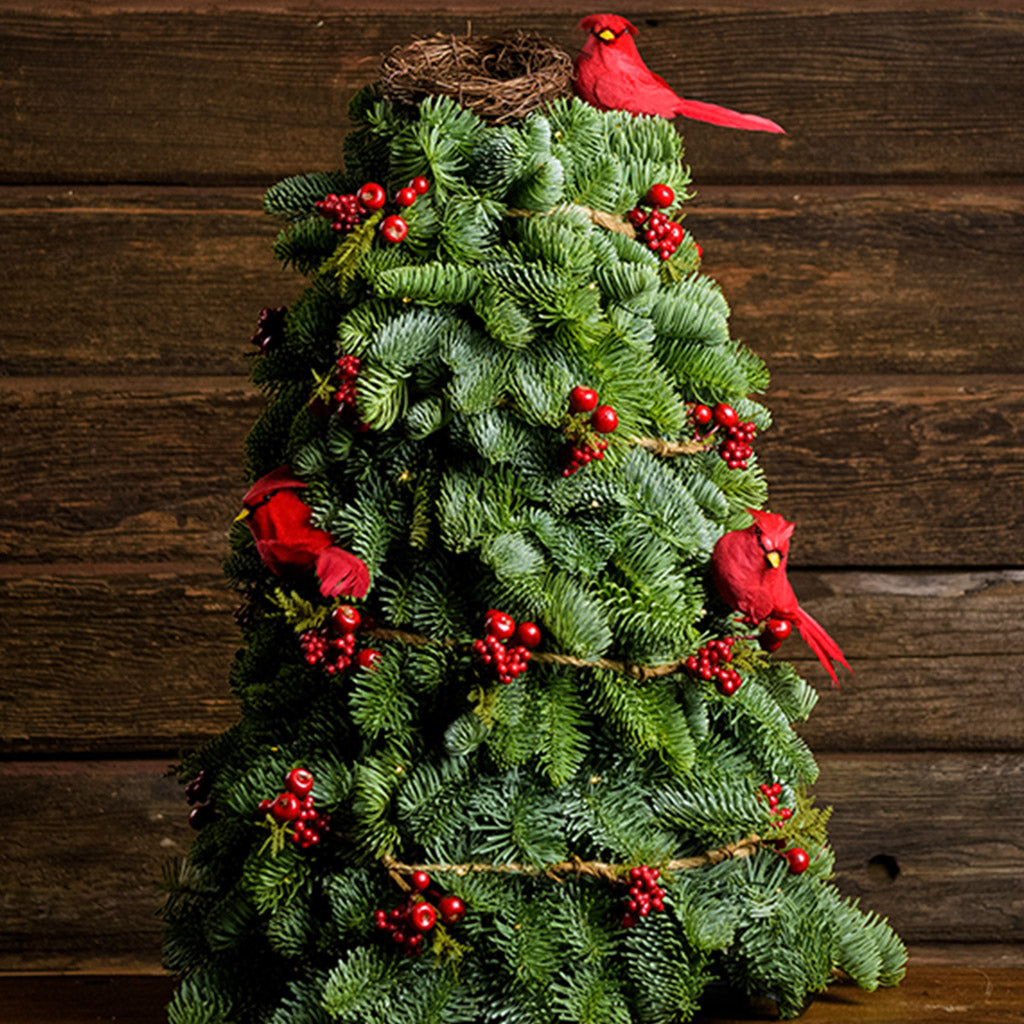 Tabletop tree of noble fir with a rustic berry garland, 3 cardinal birds, and a nest with a wood background