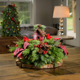 A holiday centerpiece of noble fir, white pine, incense cedar, natural pinecone, red berry & red ball clusters, 2 cardinal birds, natural stick clusters, a plaid birdhouse, and 2 tartan bows accented with a wood round on a counter. 