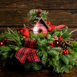 A holiday centerpiece of noble fir, white pine, incense cedar, natural pinecone, red berry & red ball clusters, 2 cardinal birds, natural stick clusters, a plaid birdhouse, and 2 tartan bows with a wood background. 