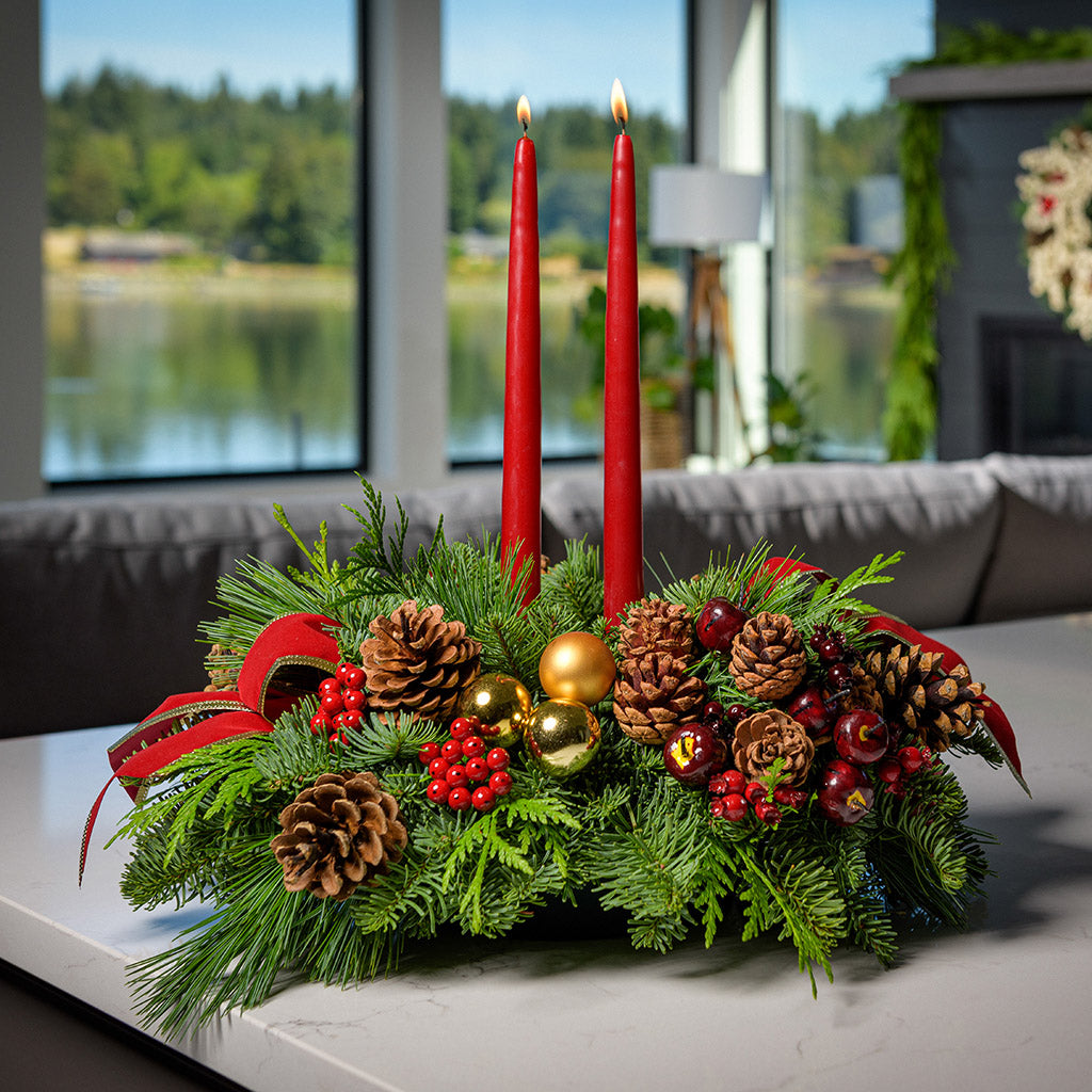 Traditional centerpiece with red balls, pine cones and berries with 2 red velveteen bows and two red taper candles on a counter.